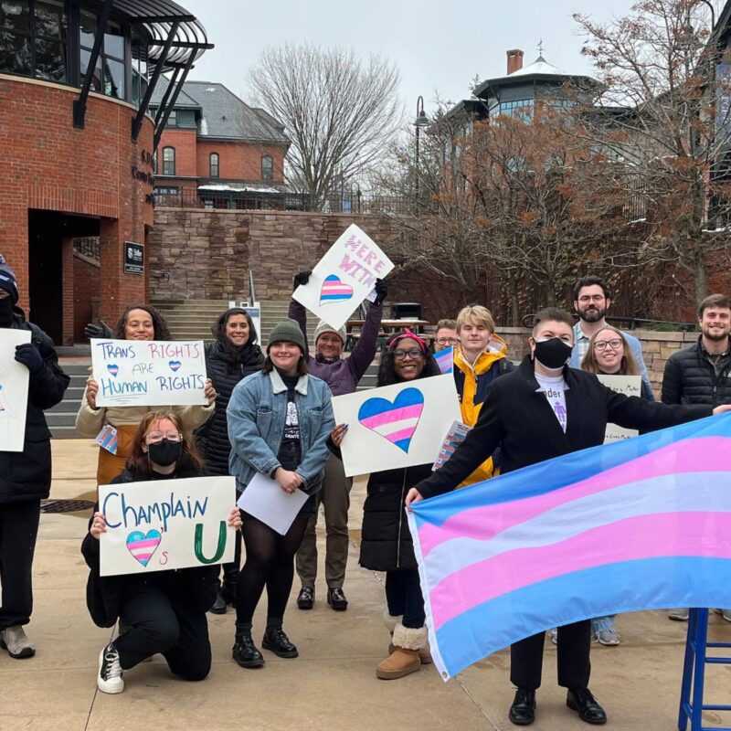 Snowy trans day of remembrance student group posing with signs and flags in the courtyard