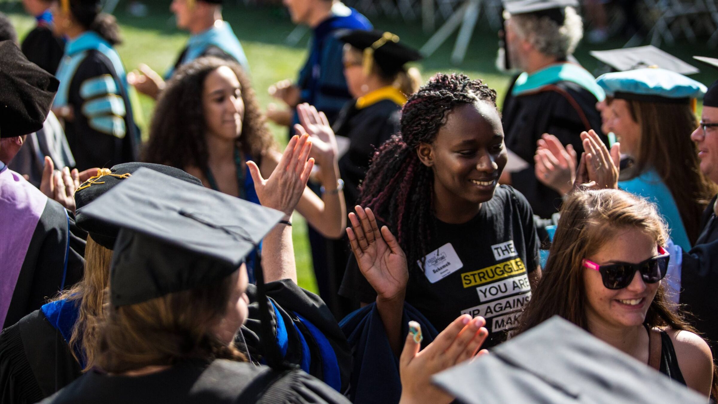 Students smiling as they walk through members of faculty wearing graduation caps high fiving each other