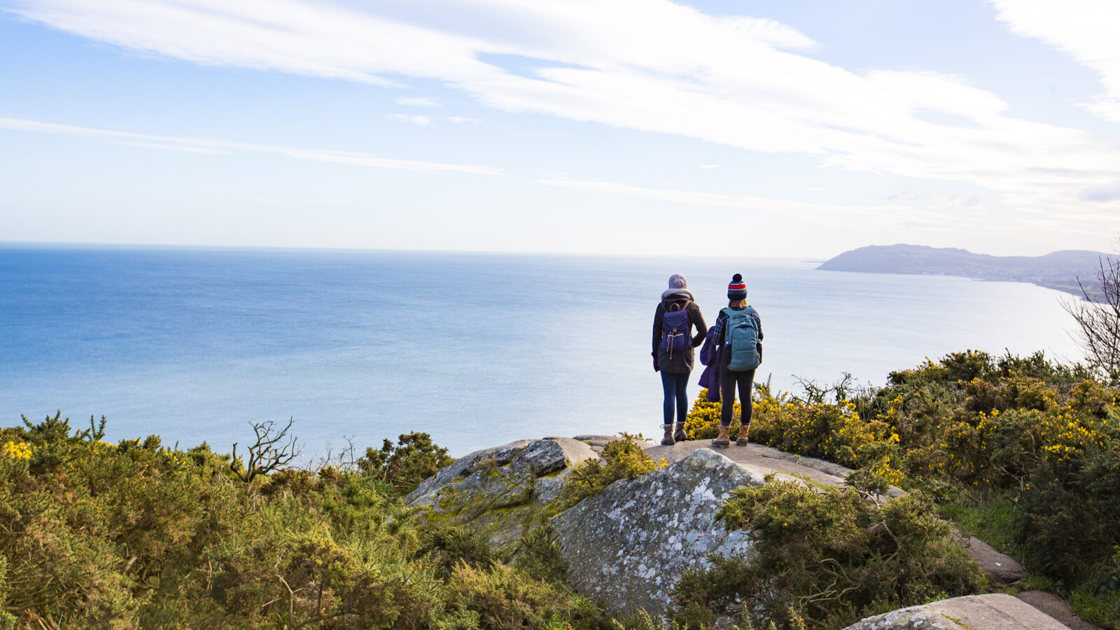 two students stand near the edge of a cliff looking out at the ocean