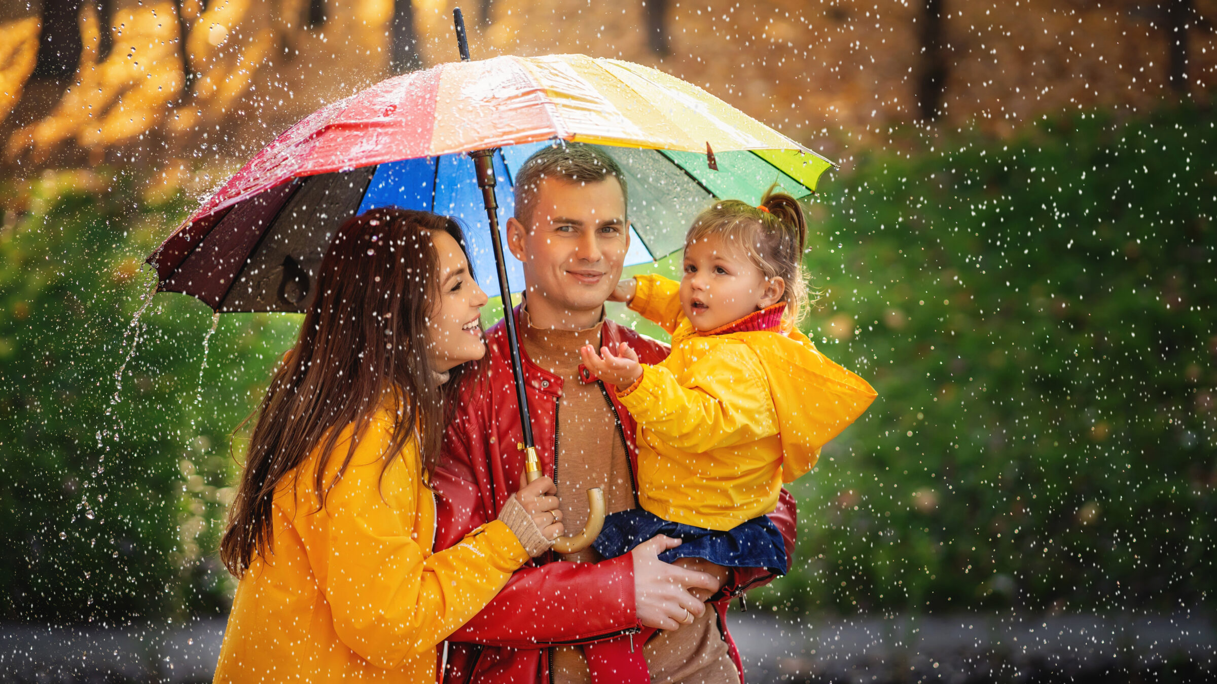 young family with colorful umbrella stands in the rain
