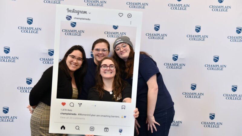 Students posing in an instagram frame with a champlain college repeated logo background