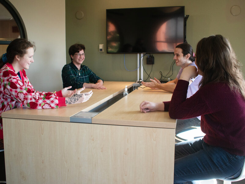 Four students sit around a table talking and laughing on the second floor of the library.
