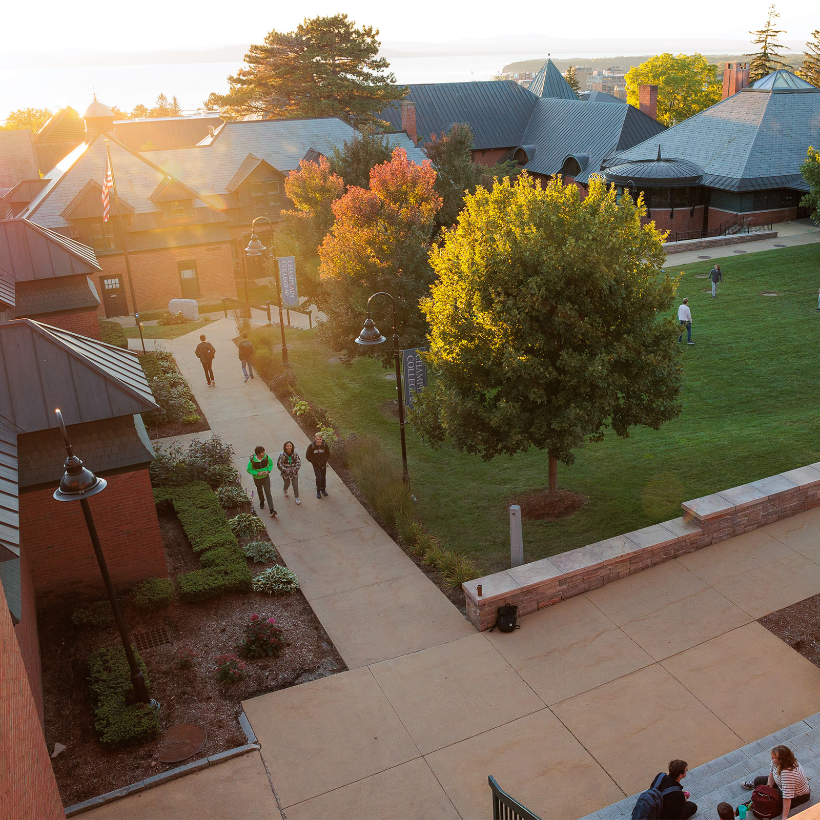 students walk alongside fall trees and campus building as the sun sets overt he lake