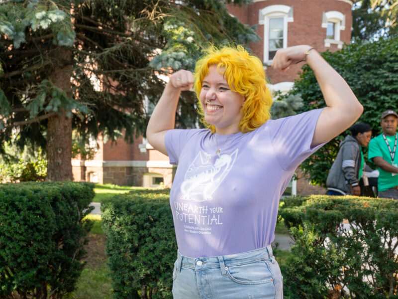 student in purple shirt and yellow hair holds their arms up in an "i'm strong" position