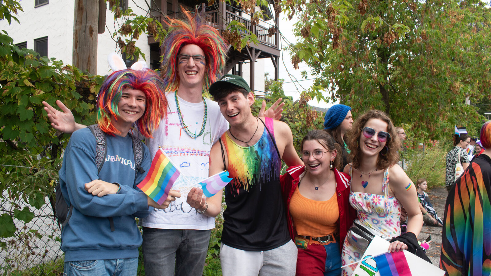 five students wearing rainbow wigs and bright colorful clothing smile during the burlington pride parade
