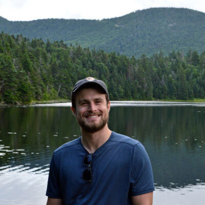 zach piper stands in front of sterling pond with beautiful green mountains and trees in the background