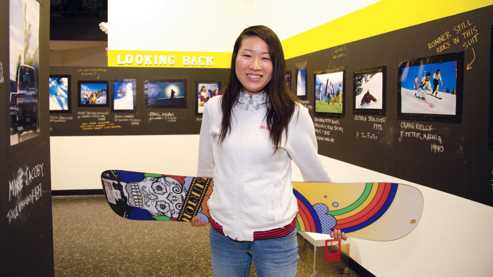 woman holds a snowboard in a hallway with graphic design art on the walls