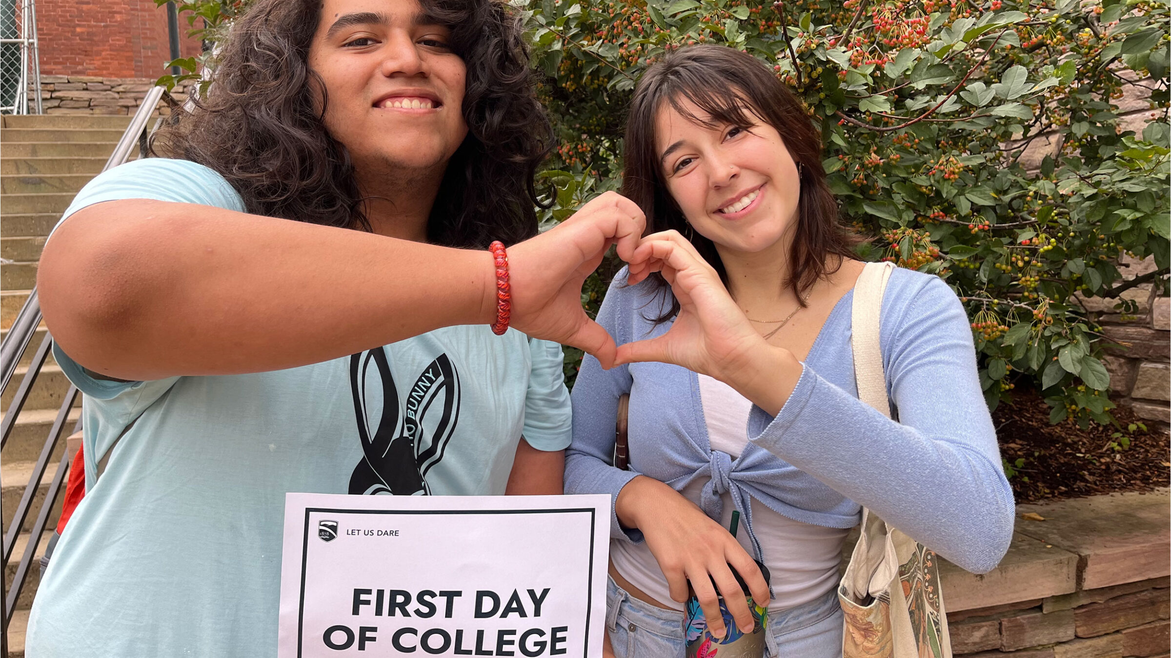 two students make a heart with their joining hands and hold up a sign that says "first day of school"