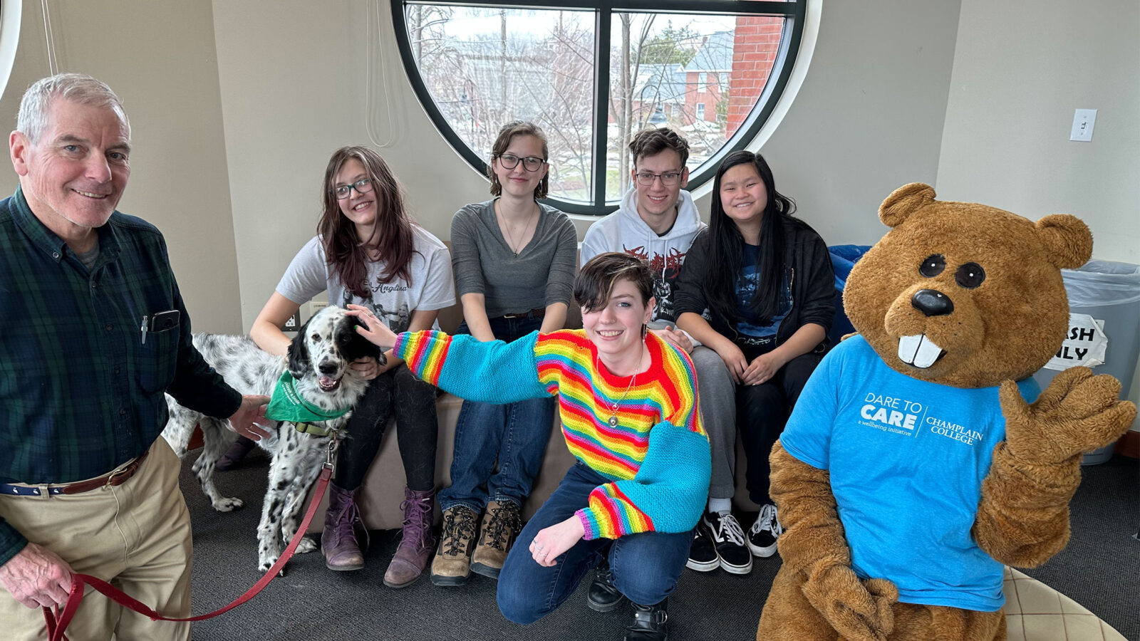 five students pose with Chauncey, a therapy dog, and the therapy dog's owner. the dog is white and black spotted.