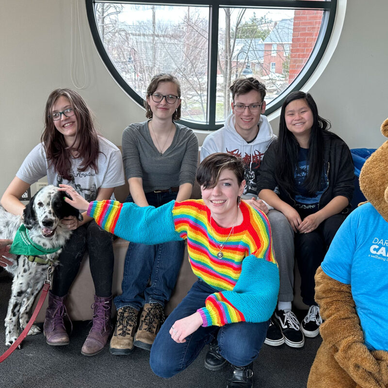 five students pose with Chauncey, a therapy dog, and the therapy dog's owner. the dog is white and black spotted.