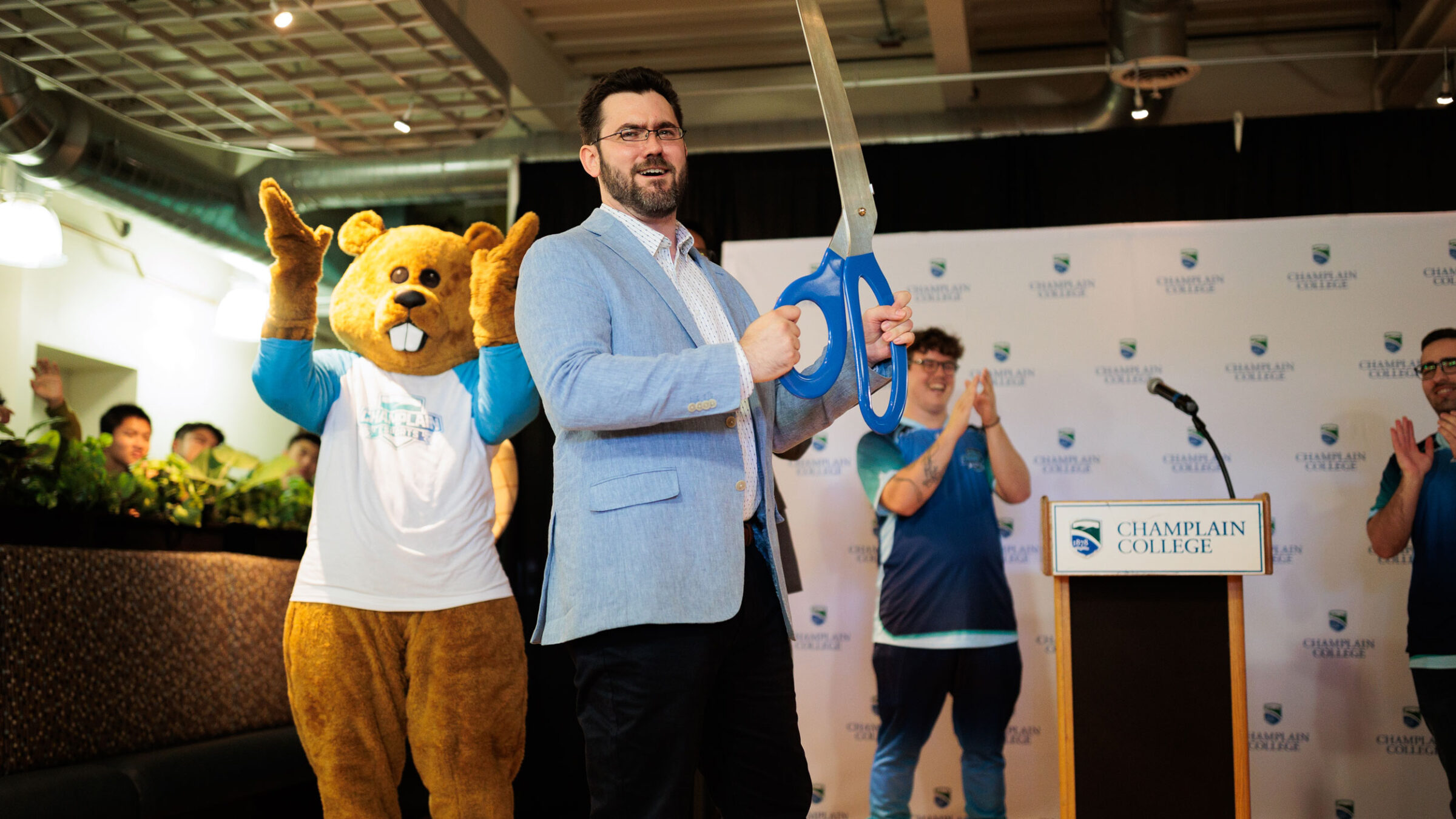 a faculty member holding large scissors, with students and Chauncy cheering