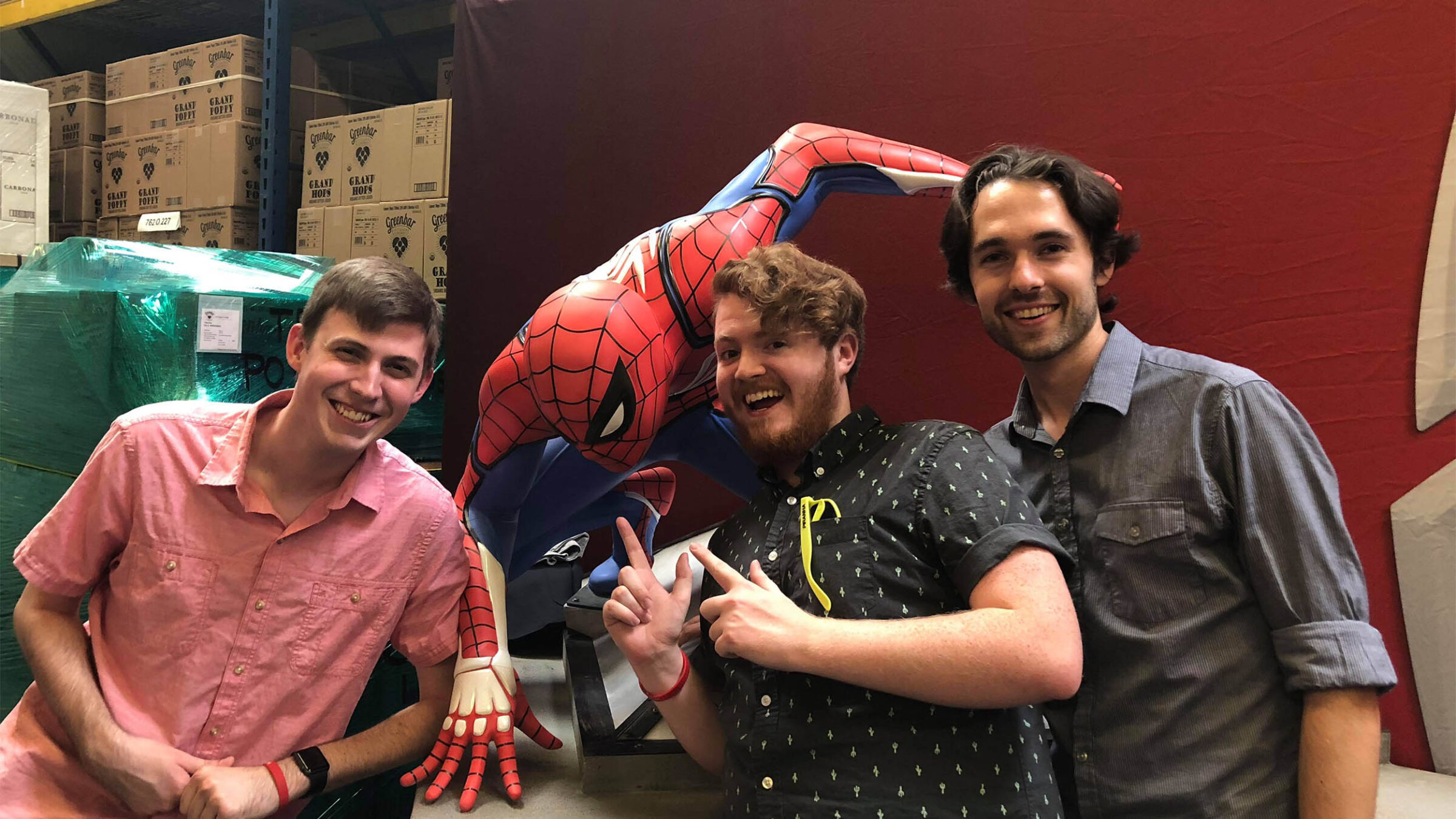 three students posing next to a statue of spider man