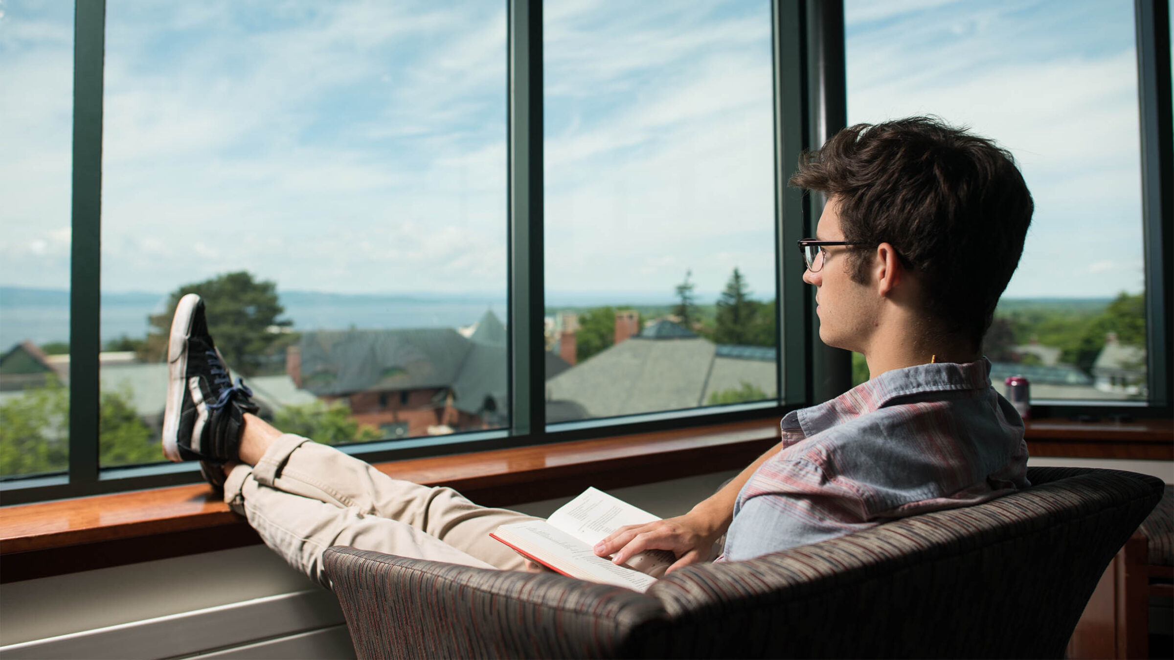 a student sitting with their feet against the window ledge with an open book in their lap