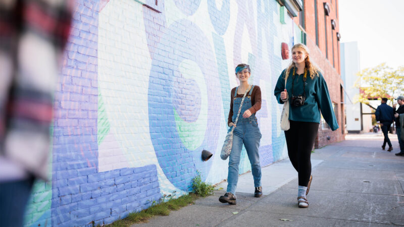 two students walk in front of a mural