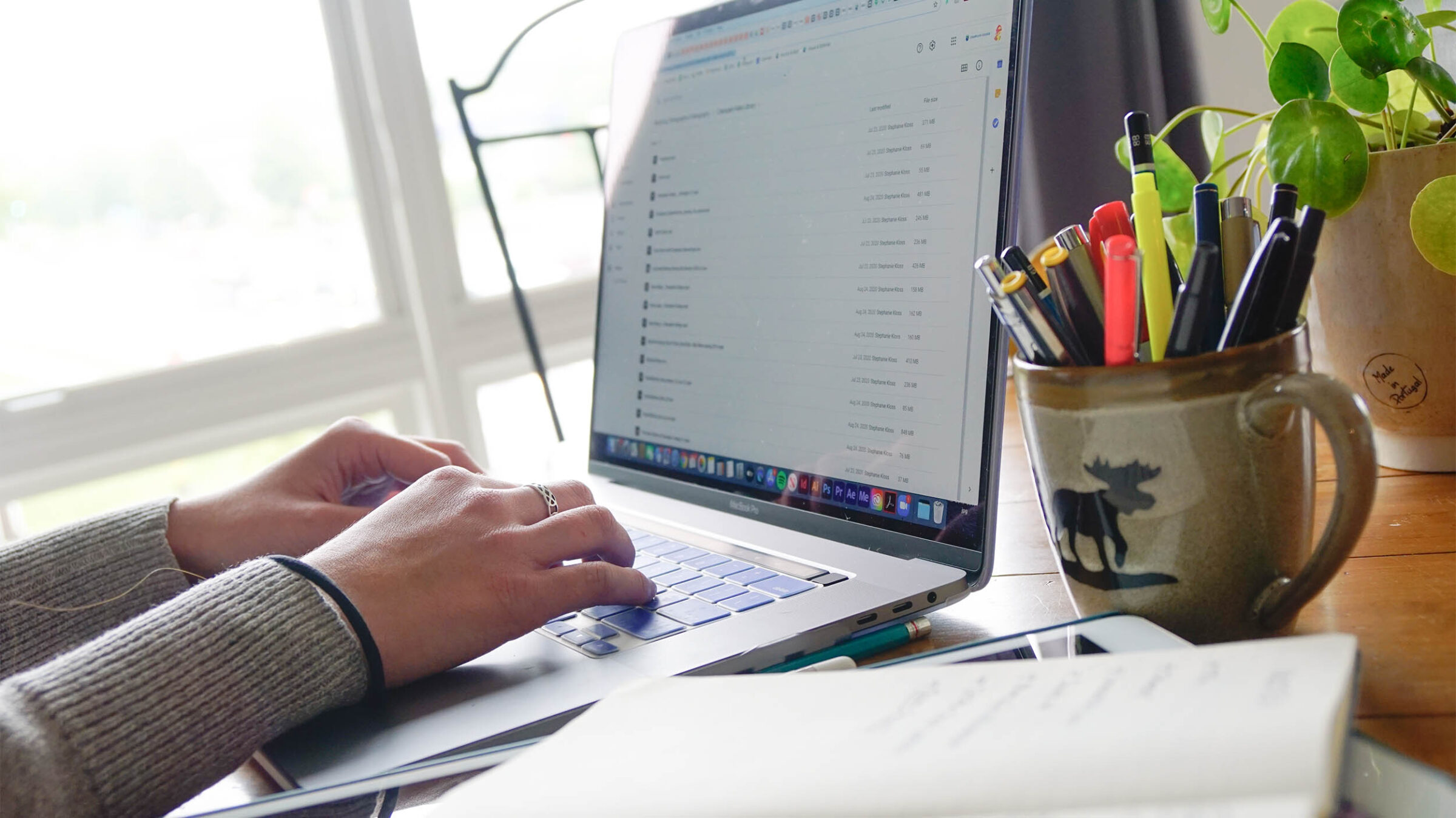 a person works on a laptop on a desk with a vermont mug holding pens
