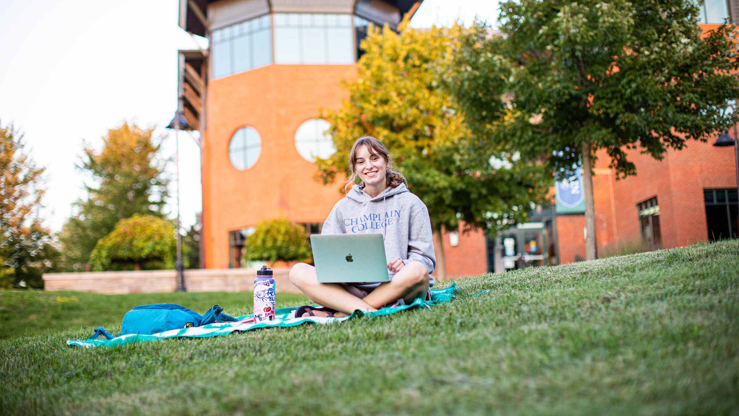 a student sitting on a blanket in the quad working on a laptop