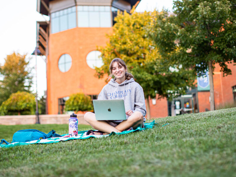 a student sitting on a blanket in the quad working on a laptop
