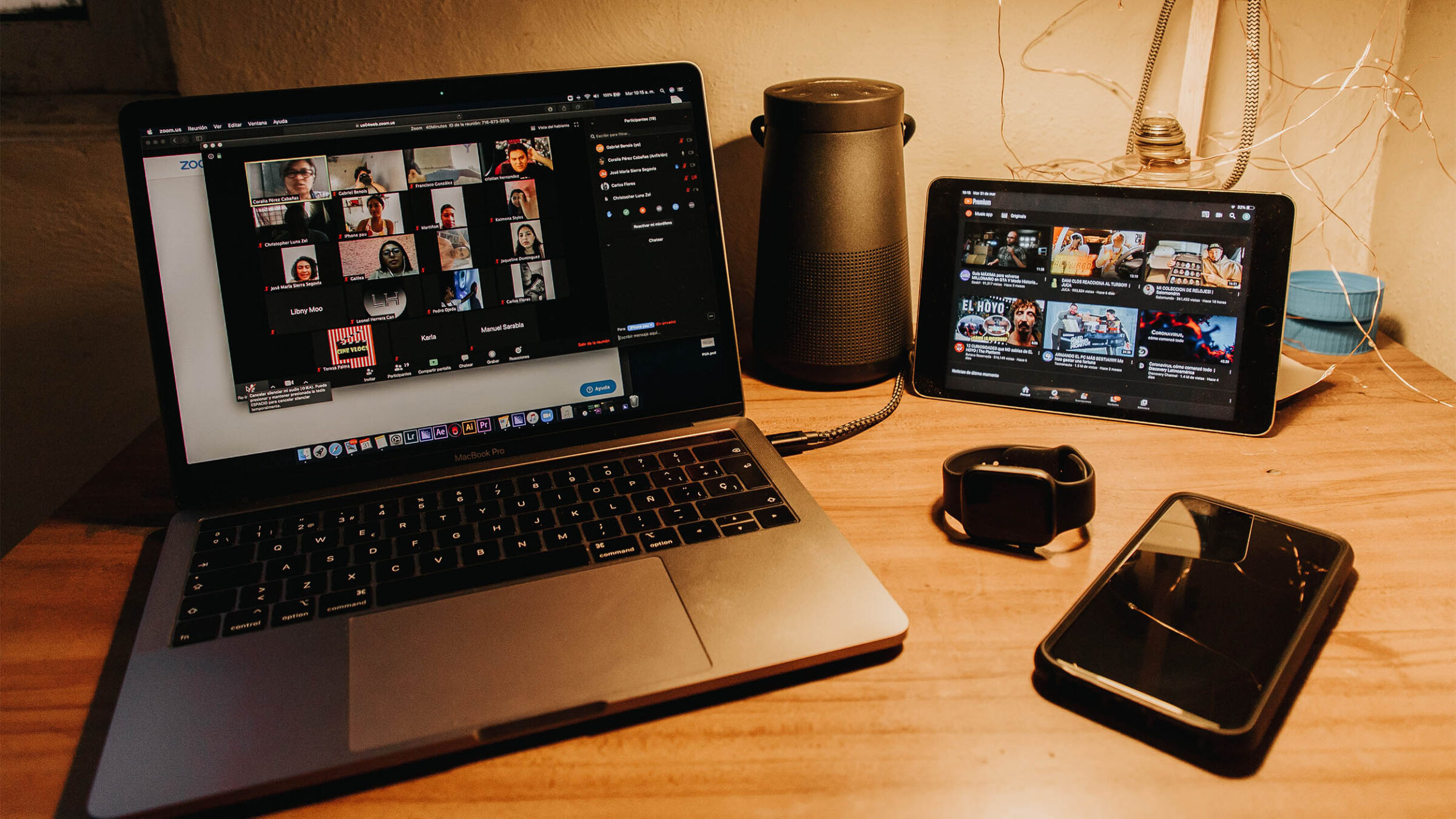 a laptop, cell phone, smart watch and ipad on a desk with an open zoom call