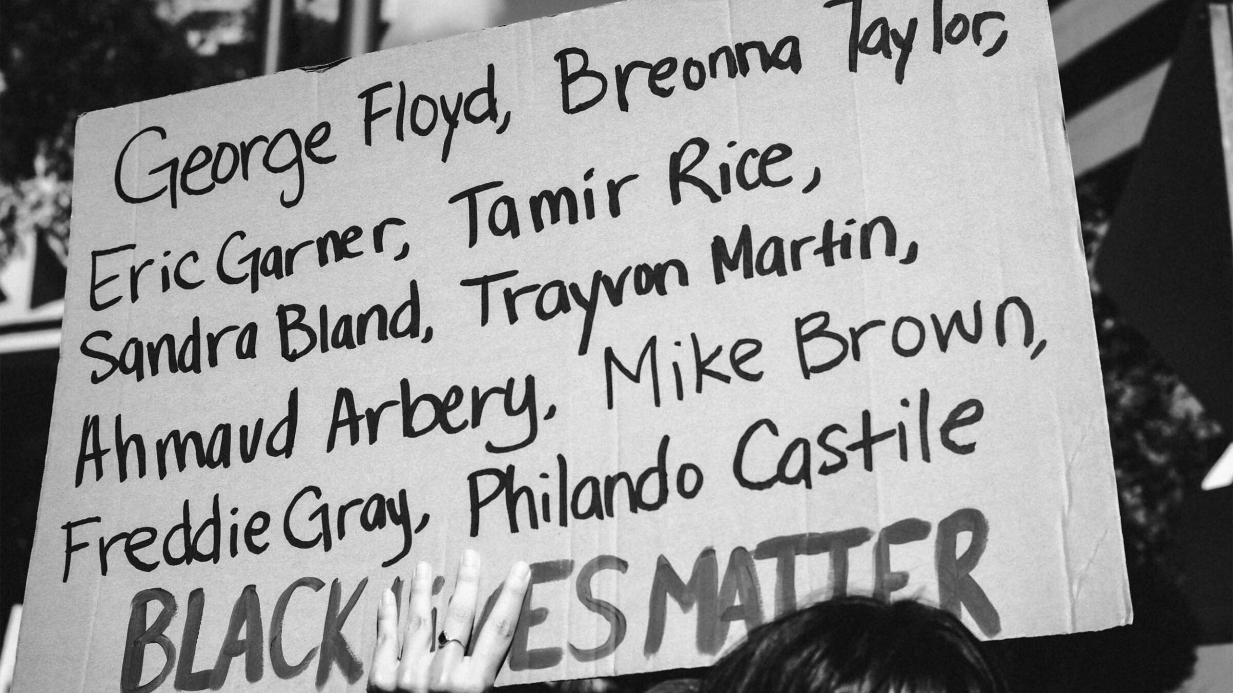 a person holding a sign with a list of names along with "Black lives matter"