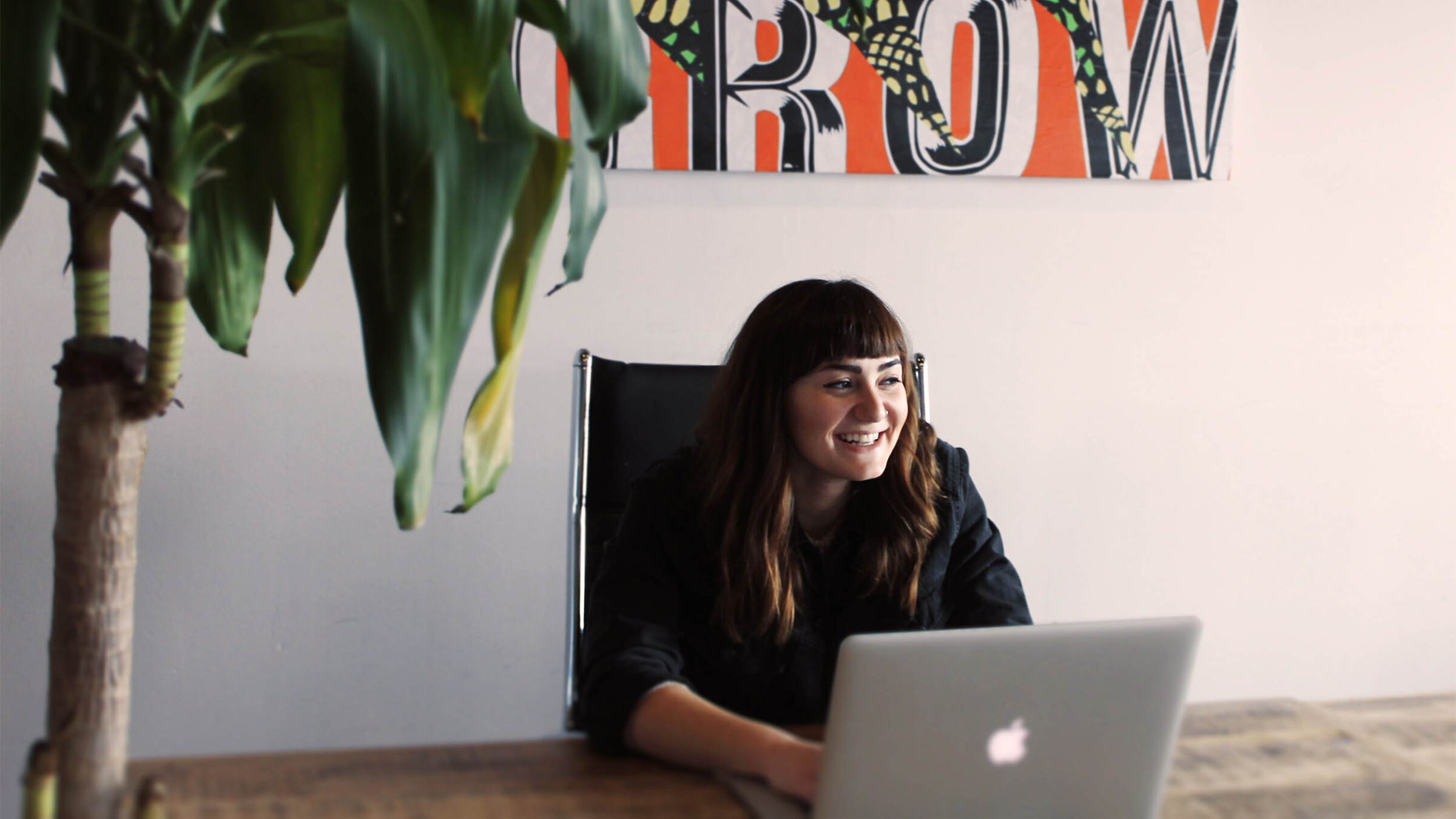 a person working on a laptop smiling. a green plant sits in the corner