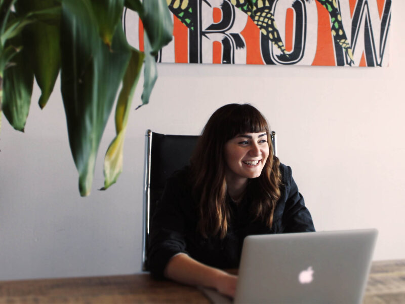 a person working on a laptop smiling. a green plant sits in the corner