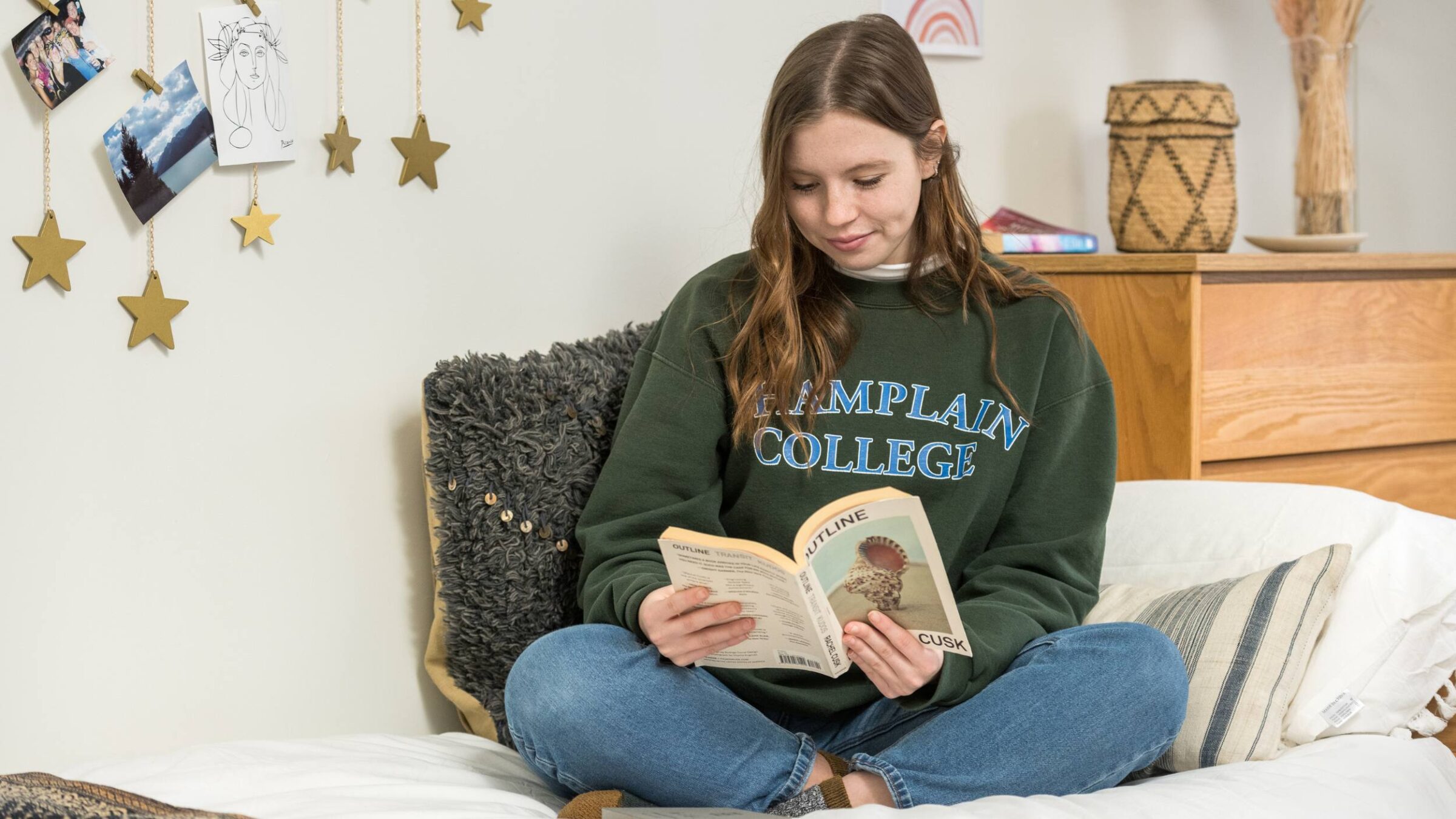 a student in a dorm room, sitting in bed reading a book