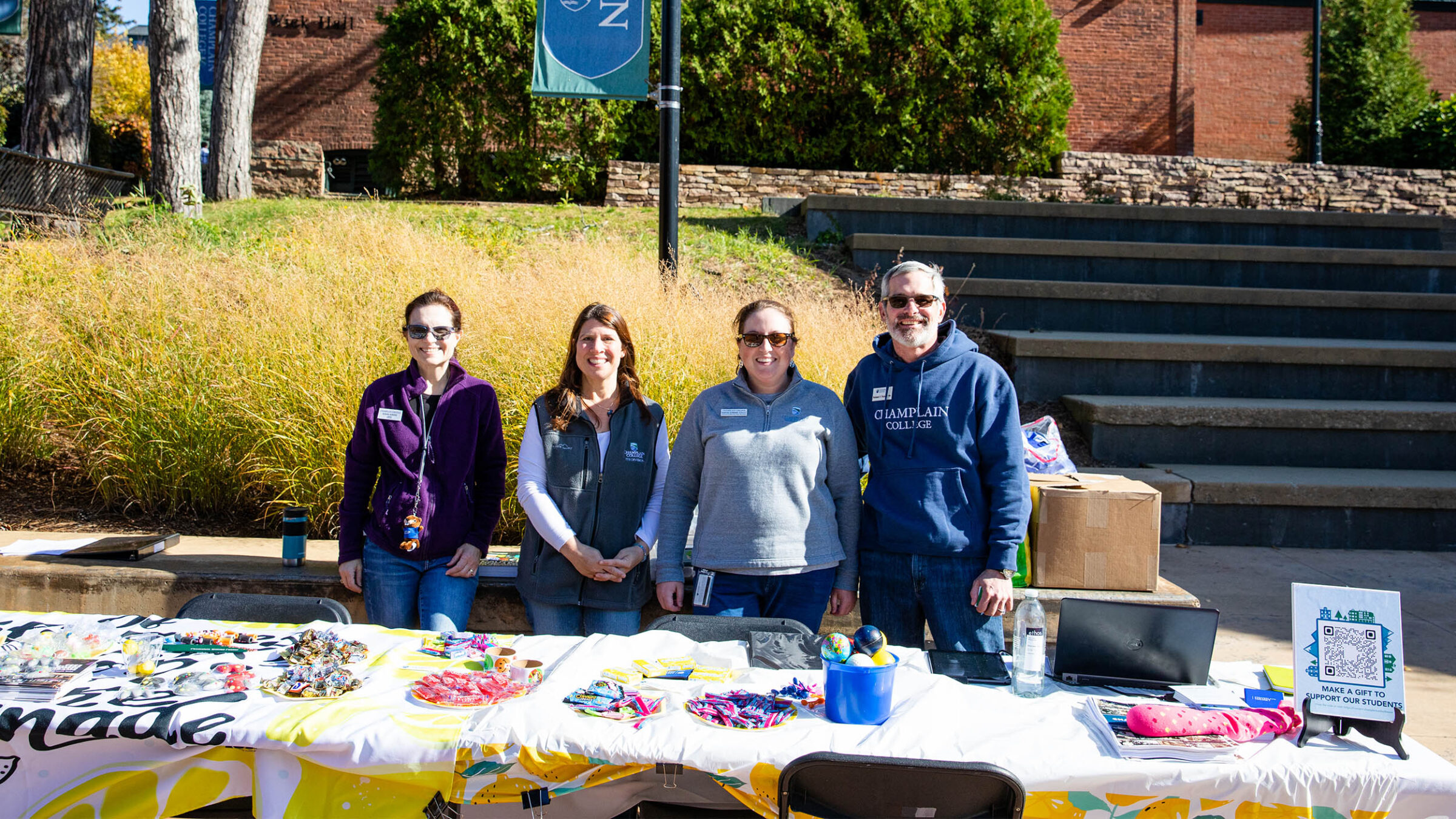 four people standing behind a table full of candy and stress balls on campus