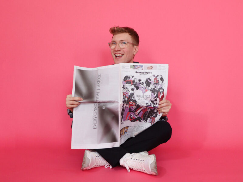 a student holding a newspaper in front of a pink background