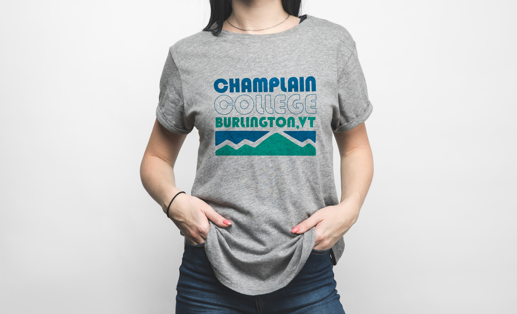 a model wearing a grey shirt with a Champlain College Burlington, VT design and blue and green mountains