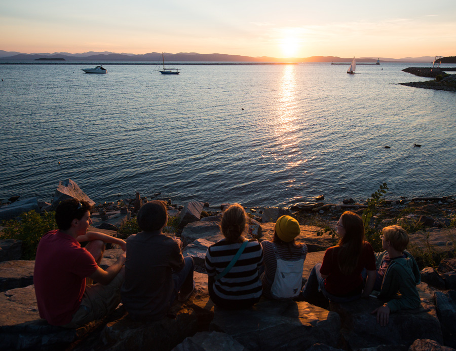 students sitting on the waterfront watching a sunset