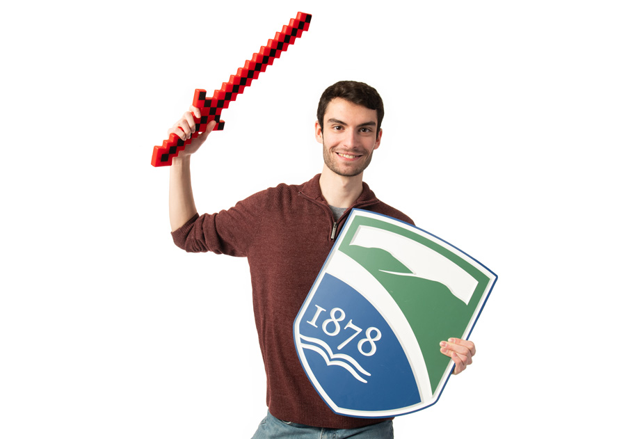 a student holding the Champlain College shield and a red pixel sword against a white background