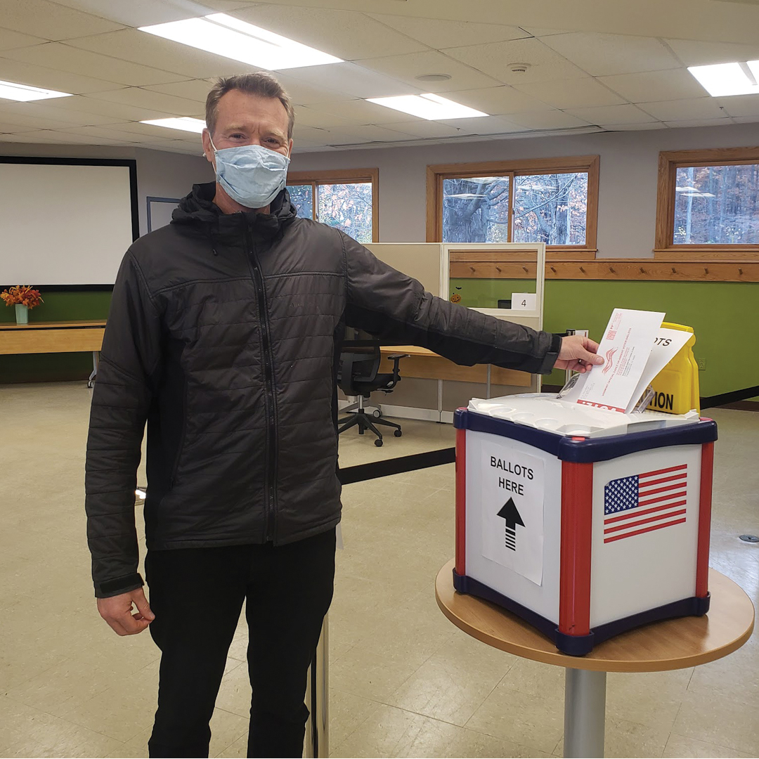 a photo of a champlain college faculty member dropping a voting ballot into the ballot box
