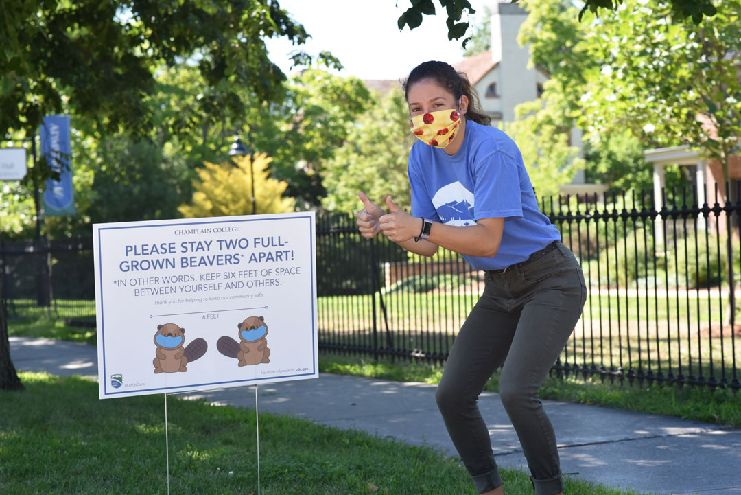 Student stands near a social distanmcing sign, giving it two thumbs-up.