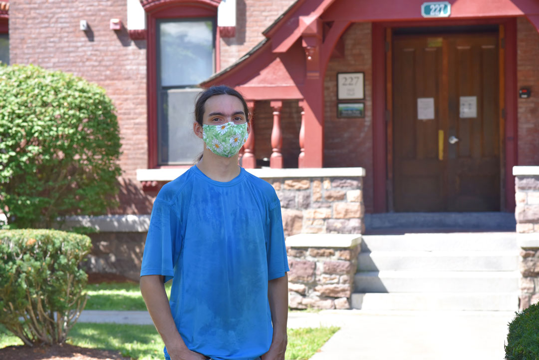 A student wearing a face mask stands in front of Hill Hall on Champlain College's campus