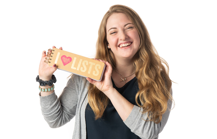 a student holding up a notepad that reads "I love lists" in front of a white background