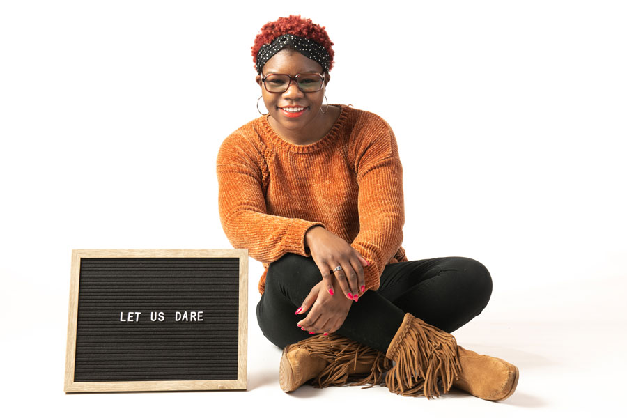 a student sitting in front of a white background with a sign reading "Let us dare" 
