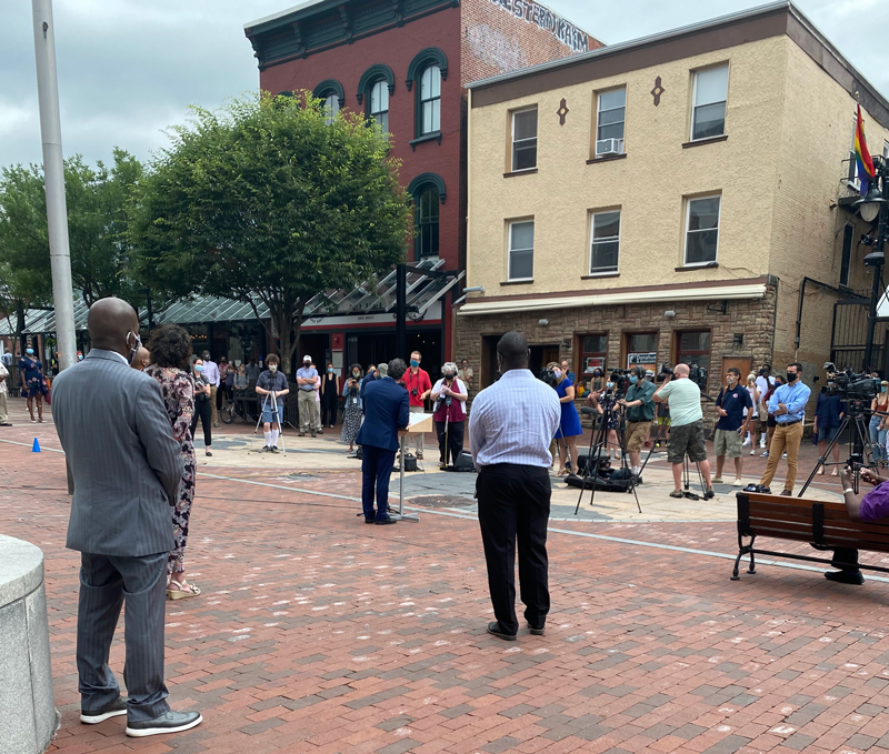 a group of people on Church Street filming a speaker talking from a podium while social distancing