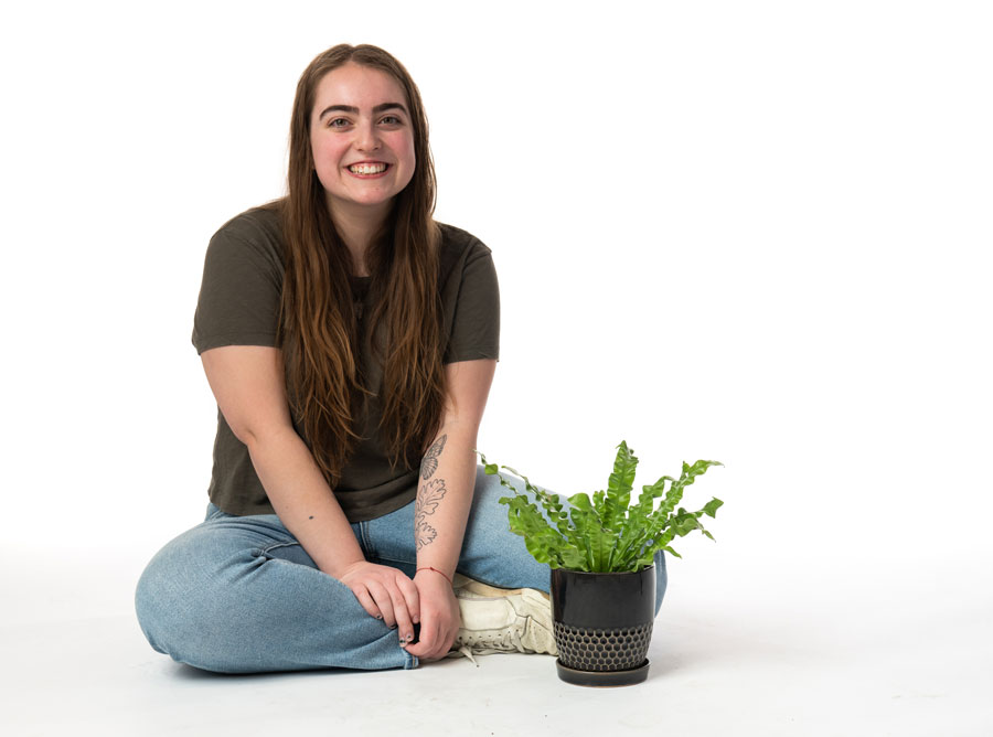 a student sitting in front of a white background with a potted plant