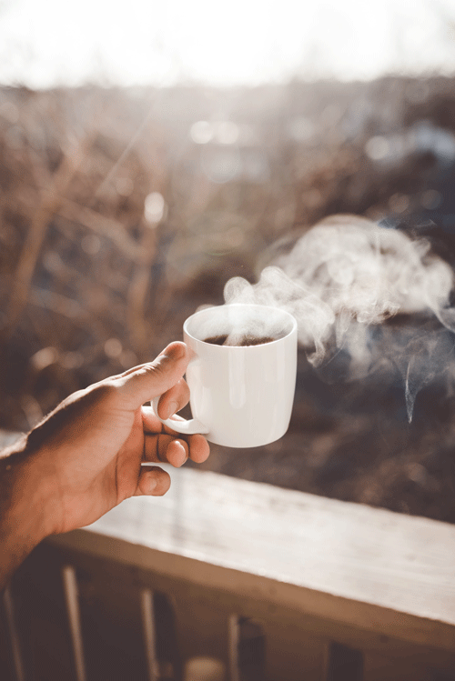a person holding a white cup of steaming coffee on a balcony 