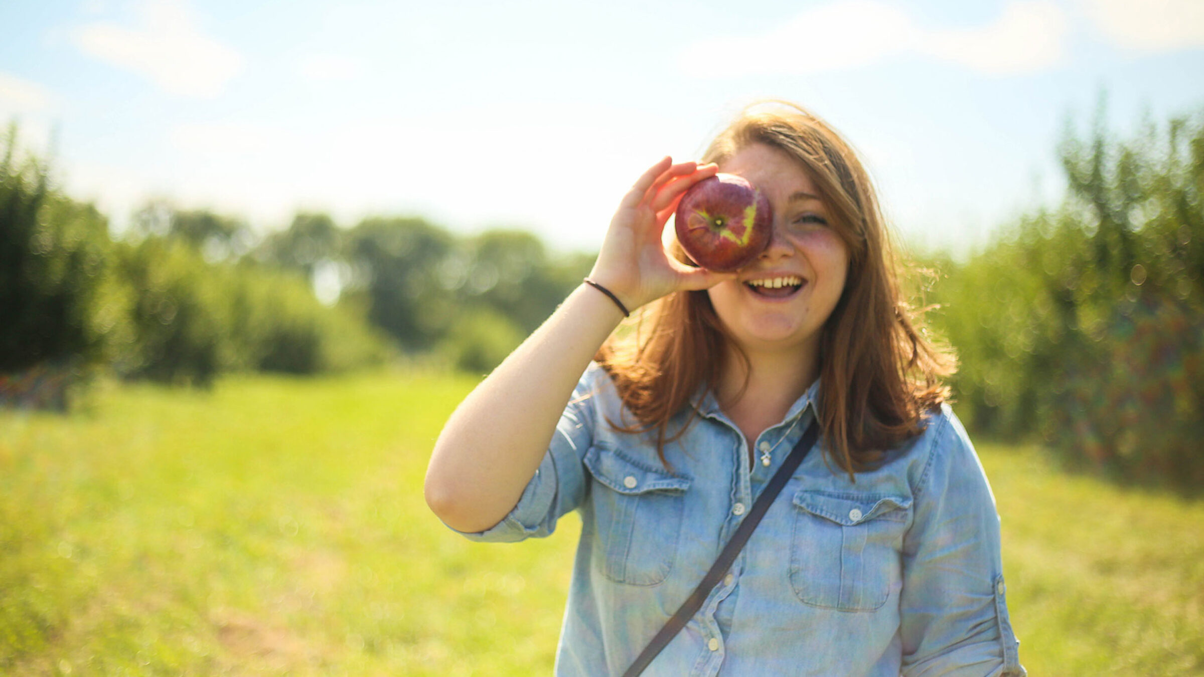 student holding an apple against their eye in a field