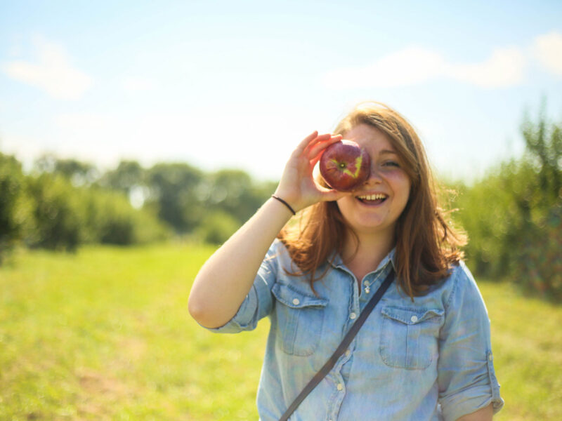student holding an apple against their eye in a field