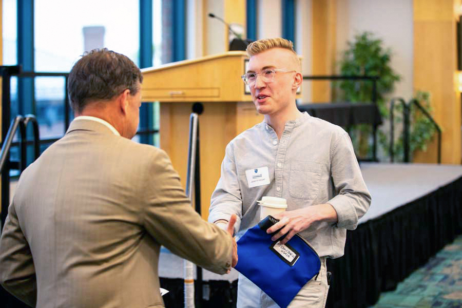 a student shaking someone's hand while holding a cup of coffee