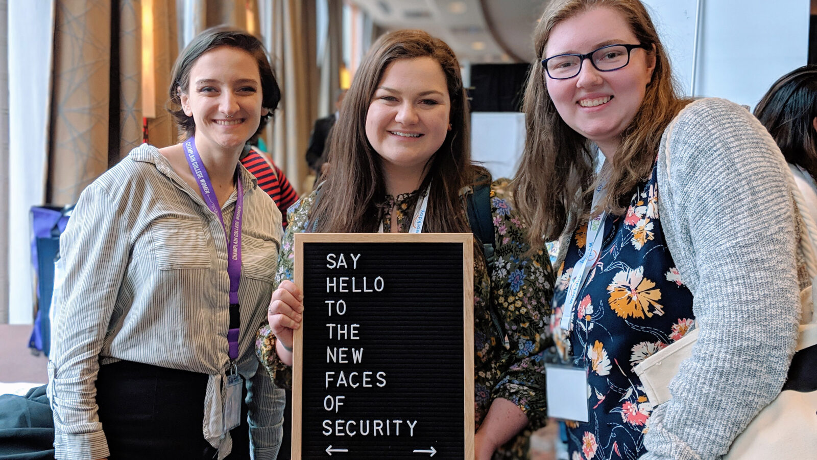 three female presenting students holding a sign that says "say hello to the new faces of security"