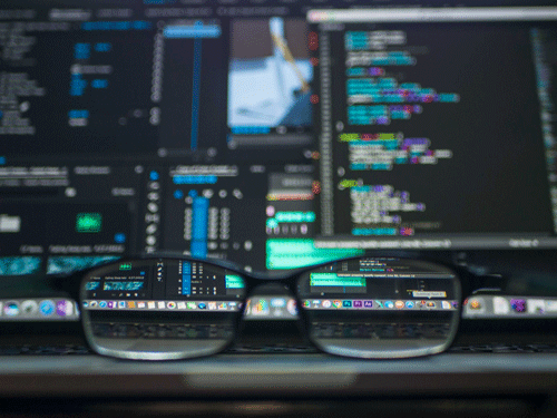 a blurred laptop screen with coding visible through a pair of glasses
