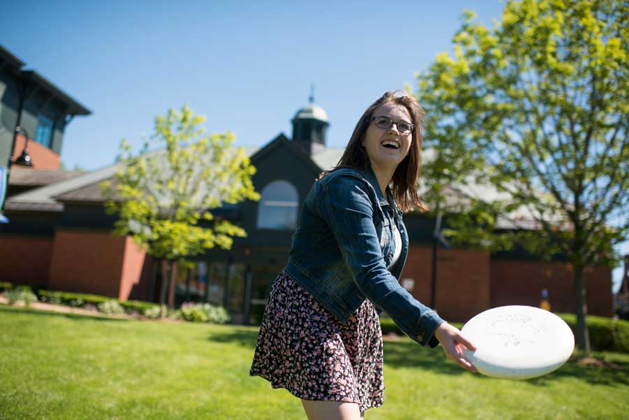 a student smiling on campus, throwing a frisbee