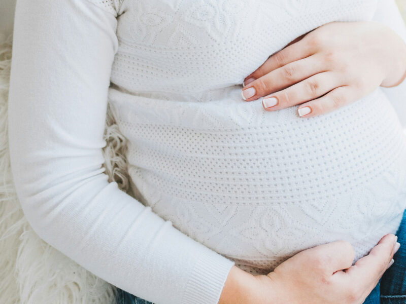 a person cradles their pregnant belly. they are wearing a white sweater and jeans.