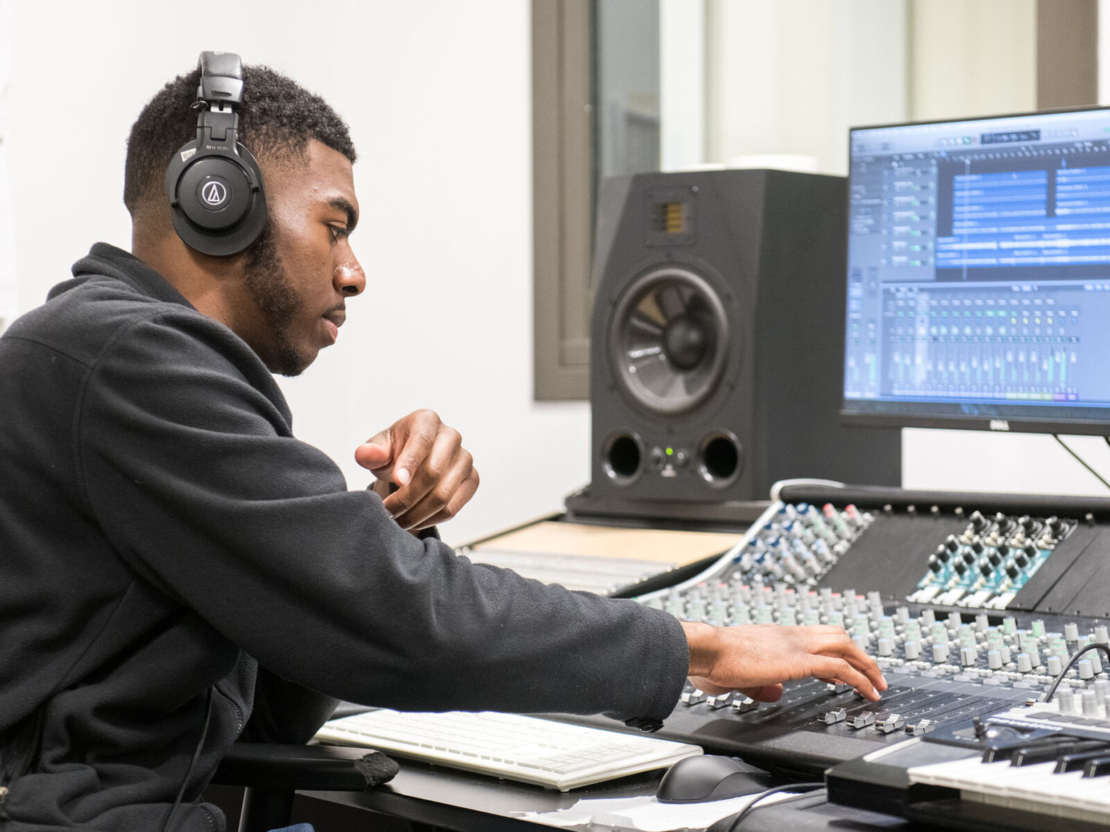 Male student wearing headphones adjusts sliders on audio equipment