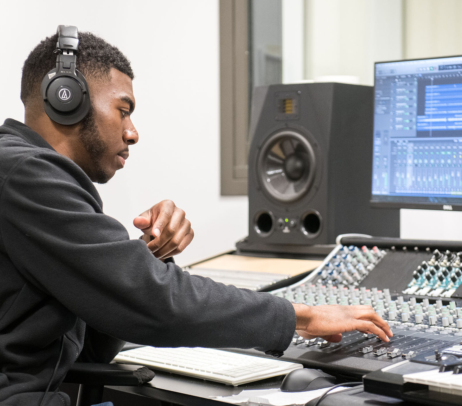 Male student wearing headphones adjusts sliders on audio equipment