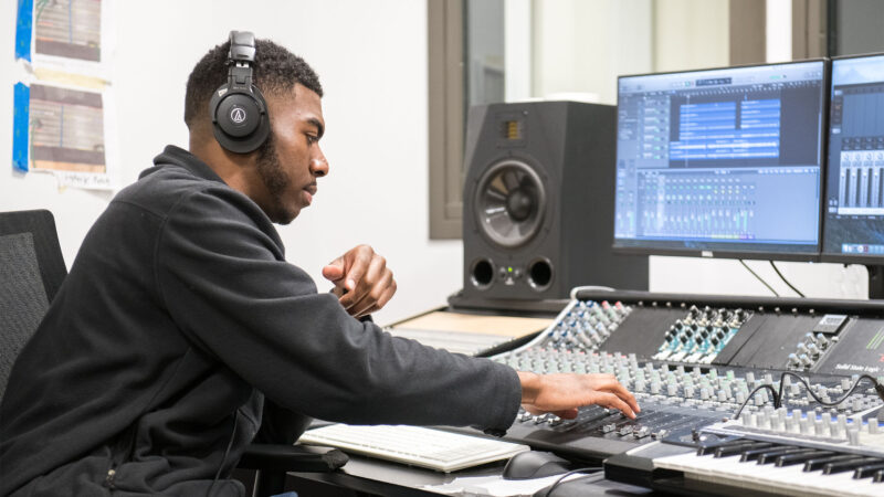 Male student wearing headphones adjusts sliders on audio equipment