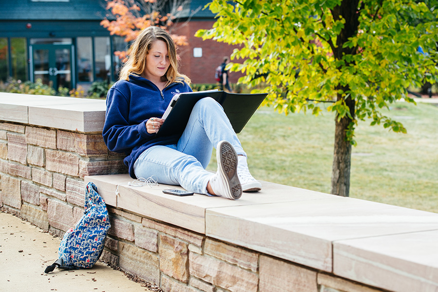 Lots of places to study. A student sitting on a brick wall studying at Champlain College in Burlington, Vermont.